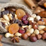 A burlap sack spilling a variety of nuts and dried fruits on a wooden table