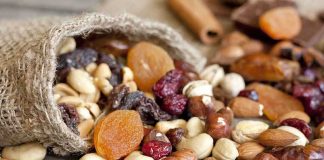 A burlap sack spilling a variety of nuts and dried fruits on a wooden table