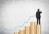 Businessman standing on stacks of coins drawing a growth chart