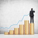 Businessman standing on stacks of coins drawing a growth chart