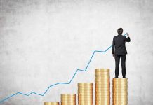 Businessman standing on stacks of coins drawing a growth chart