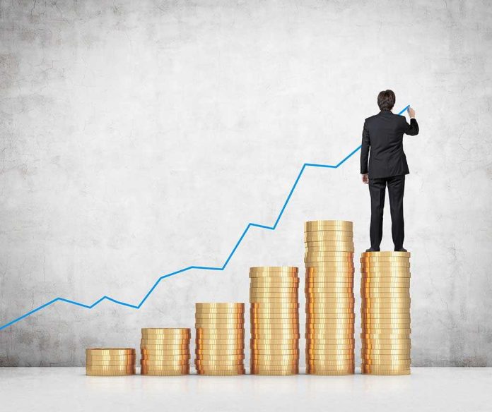 shutterstock_221639947.jpg Businessman standing on stacks of coins drawing a growth chart