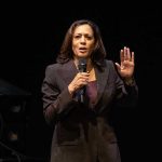 Person speaking into microphone with hand raised.