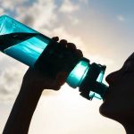 Silhouette of person drinking from a water bottle.
