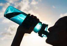 Silhouette of person drinking from a water bottle.