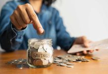 Person placing a coin into a savings jar labeled 'SAVINGS'