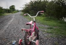Parents Vanish! — Child Left to FEND FOR HIMSELF Pink childrens bike with training wheels on gravel path.