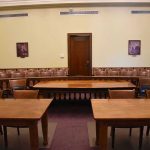 BOMBSHELL TESTIMONY — Biden Insider’s Shocking Admission Empty courtroom with wooden tables, chairs, and a door.