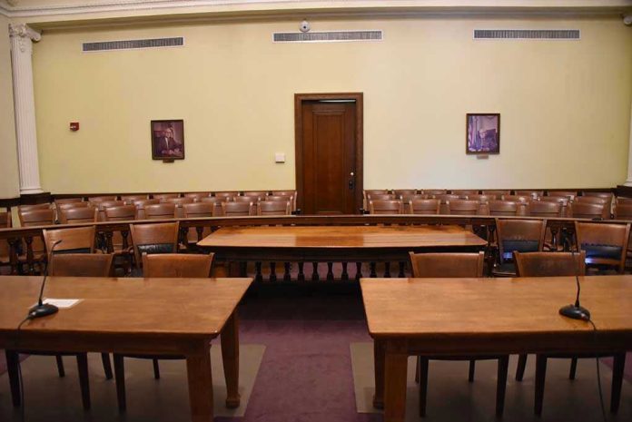 1291095706 Empty courtroom with wooden tables, chairs, and a door.