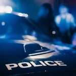 Police AMBUSHED Responding to Bullet-Riddled Car Police car with blurred figures in the background.