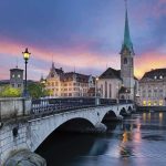 Switzerland UNLEASHES Ultimate Citizen Protection Plan Scenic view of Zurich with a bridge, historic buildings, and a sunset sky
