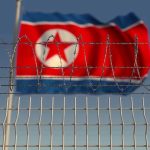 North Korea Hacks U.S. Paychecks—Nobody Stopped It Barbed wire fence with North Korean flag behind.