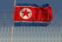 North Korea Hacks U.S. Paychecks—Nobody Stopped It Barbed wire fence with North Korean flag behind.