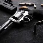 SELF-DEFENSE BACKFIRES: 7-Eleven Termination Sparks Fury Revolvers and bullets on a dark surface.