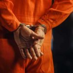 Kristi Noem CATCHES 150 Sex Offenders Person in orange jumpsuit with handcuffs behind back.