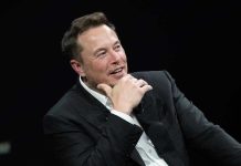Musk’s AI Bot Calls Him Greatest Human—Chaos Ensues Man in suit smiling, resting chin on hand.