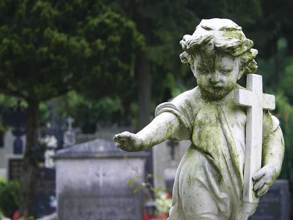Weathered statue of a child angel holding a cross in a cemetery