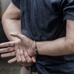Trusted Teacher ARRESTED – Child Abuse Charges Shock Community Person in handcuffs with hands behind back.