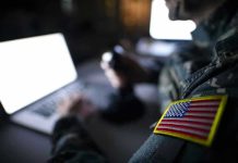 Missile Defense SHOCK Upgrade Reshapes U.S. Power Soldier using laptop with US flag patch visible.