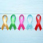 Aging Reversal Twist Hiding In Cancer Lab Colorful awareness ribbons on light wooden background.