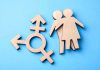 Sex Definition War Hits Schools Again Wooden transgender symbol and couple figures on blue background.