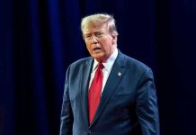 Trump’s Insurrection Act Threat Very Real Man in suit with red tie speaking on stage.