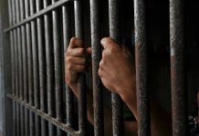 Prison Time for Questioning the Powerful Hands gripping prison cell bars tightly.