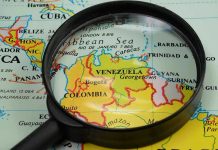 Maduro’s Inner Circle Finally Faces U.S. Justice Magnifying glass focusing on Venezuela and Colombia on map.