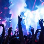 Lady Gaga Stops Concert for Immigration Tirade Crowd at a concert with hands raised and smoke effects in the background