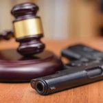 Biden Released Him, Now A Woman is Dead Gavel and handgun on a wooden surface.