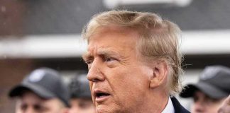 King Charles’s US Visit Sparks Backlash Man in suit and red tie speaking outside.