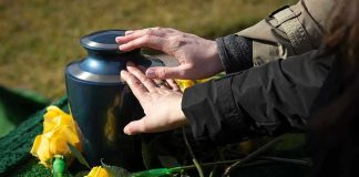 Canada Kills 26-Year-Old for Blindness Hands touching an urn surrounded by yellow roses.