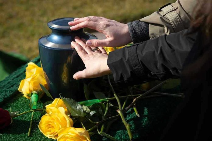 1298533777 Hands touching an urn surrounded by yellow roses.