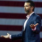 Trump Jr. To Host Apprentice? Amazon’s Bold Move Man speaking in front of American flag backdrop.