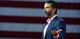 Trump Jr. To Host Apprentice? Amazon’s Bold Move Man speaking in front of American flag backdrop.