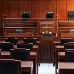 DOJ CONFRONTED: Billionaire’s Name Hidden in Epstein Files Empty courtroom with wooden furniture and black chairs.