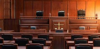 DOJ CONFRONTED: Billionaire’s Name Hidden in Epstein Files Empty courtroom with wooden furniture and black chairs.