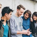 Harvard Flags Alarming Drop In Teen Hangouts Group of friends looking at a smartphone.