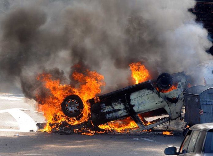 shutterstock_137895923 An overturned car engulfed in flames and smoke on a city street