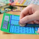 Lottery WIN—Generosity Pays $586K Reward! A person scratching off a bingo lottery ticket with a coin