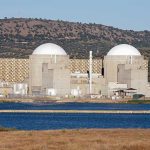 Drone Strike Ignites Nuclear Plant Fire Nuclear power plant with domed structures beside a water body and mountains in the background