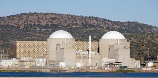Drone Strike Ignites Nuclear Plant Fire Nuclear power plant with domed structures beside a water body and mountains in the background