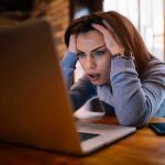 Mystery Codes Flood Inboxes — What’s Microsoft Hiding? Woman frustrated at laptop, holding her head.
