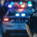 Pre-Dawn MASS SHOOTING — MANHUNT Launched! Police officer with patrol car and flashing lights.