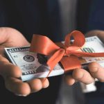 Trillion $$ BOON For AMERICA — Where it’s GOING Hands holding stack of hundred-dollar bills with ribbon.