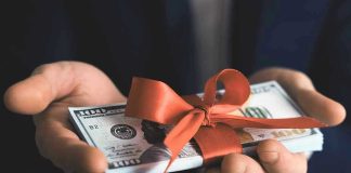 Trillion $$ BOON For AMERICA — Where it’s GOING Hands holding stack of hundred-dollar bills with ribbon.