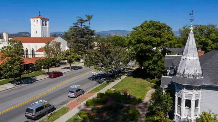 1864730230-1 Street with church, parked cars, and trees.