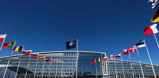 Nuclear Line ERASED — Finland Blinks Flags outside NATO headquarters building under clear blue sky.