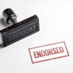RISKY ENDORSEMENT— Schumer Doubles Down Rubber stamp with ENDORSED text on paper.