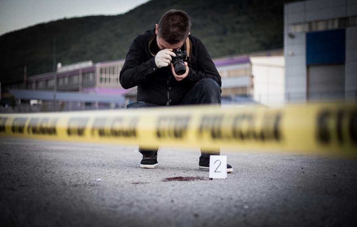 702059647-1 Crime scene photographer behind police tape with evidence marker.
